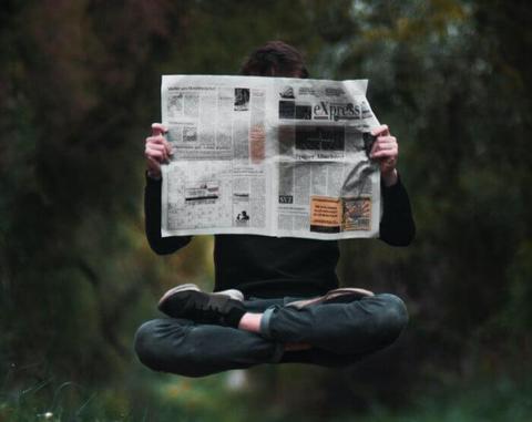 Levitating man with his legs crossed, reading a newspaper